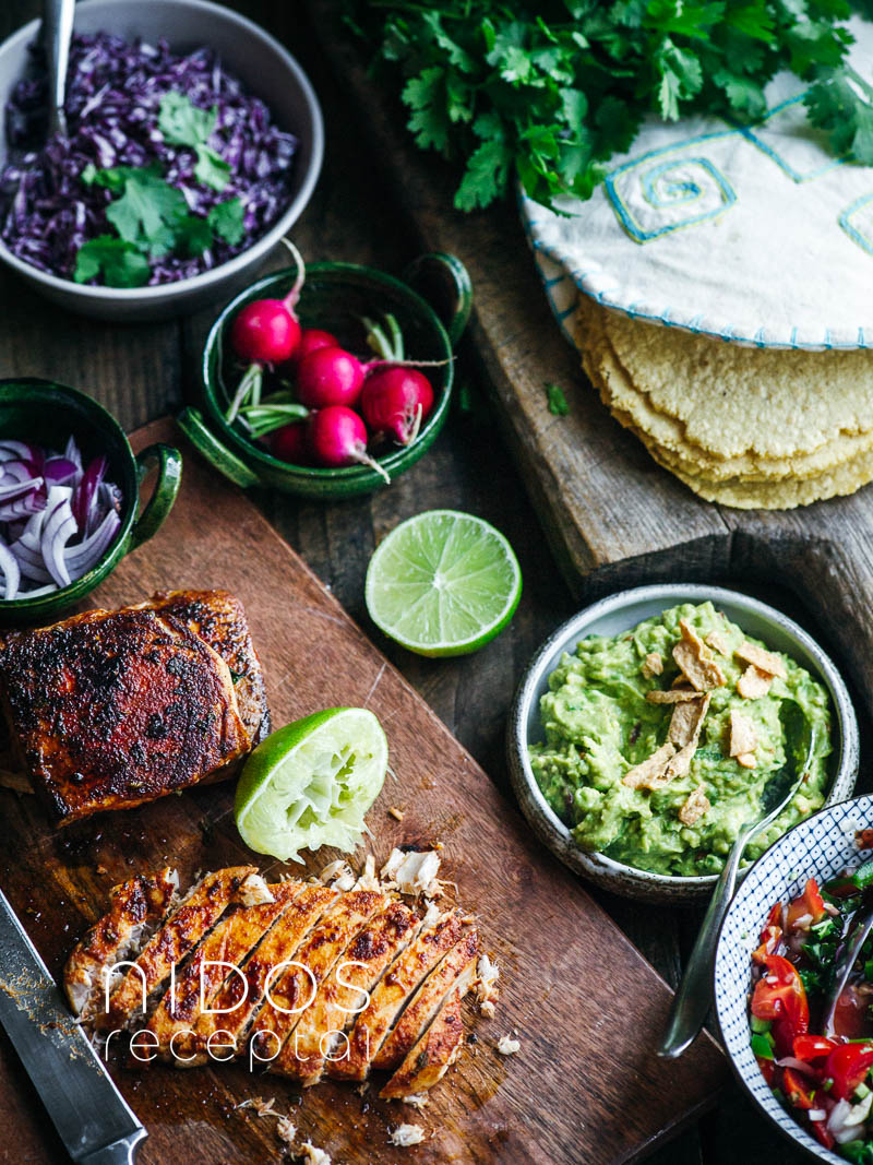 mexican table with tortillas, fish, guacamole and tomatos